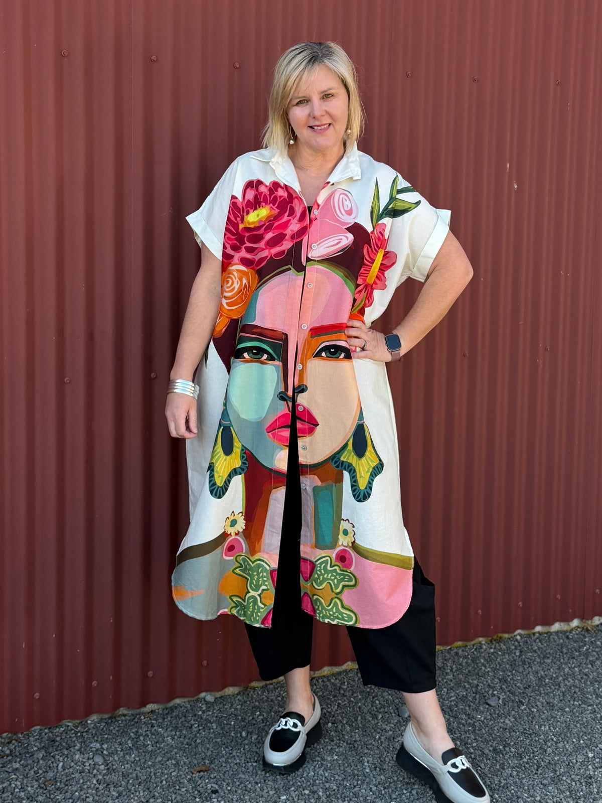 A true statement piece that’s bursting with personality. This longline shirt features a striking artistic face and floral print in vibrant pink, orange and green tones against a fresh white background.  Label Cindy C