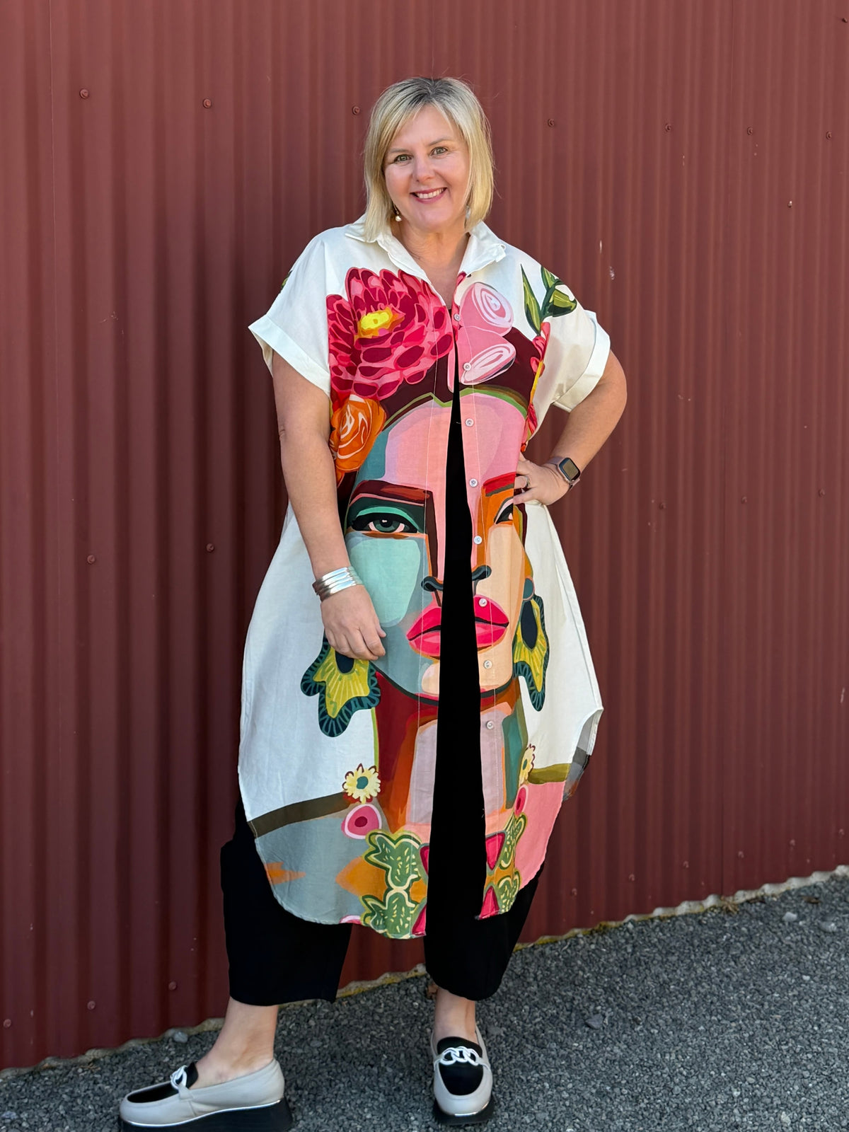 A true statement piece that’s bursting with personality. This longline shirt features a striking artistic face and floral print in vibrant pink, orange and green tones against a fresh white background.  Label Cindy C