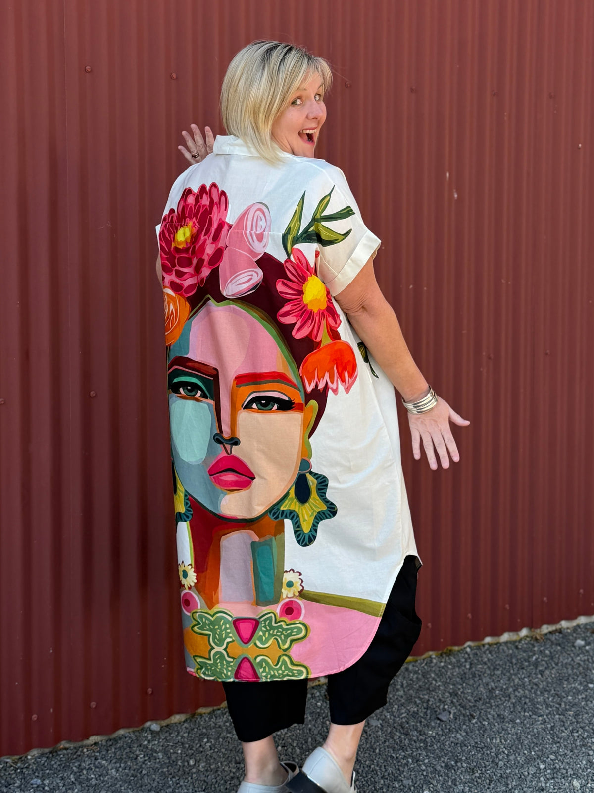 A true statement piece that’s bursting with personality. This longline shirt features a striking artistic face and floral print in vibrant pink, orange and green tones against a fresh white background.  Label Cindy C